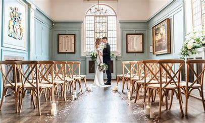 Photo of a wedding couple standing at the front of an aisle in a blue hall