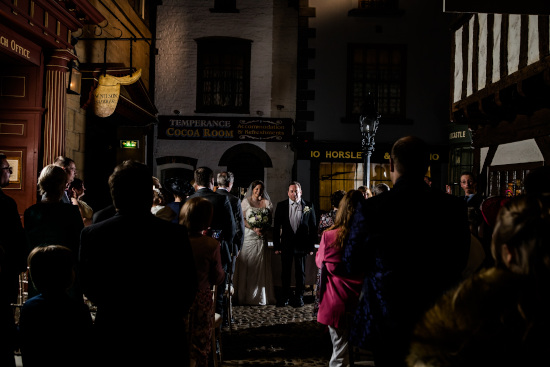 Bride and groom stand at the end of the aisle inside York Castle Museum and smile at their guests who stand and clap