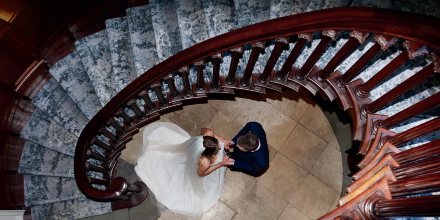 A view of a bride and groom who are stood in the centre of a large circular staircase, from above looking down on them