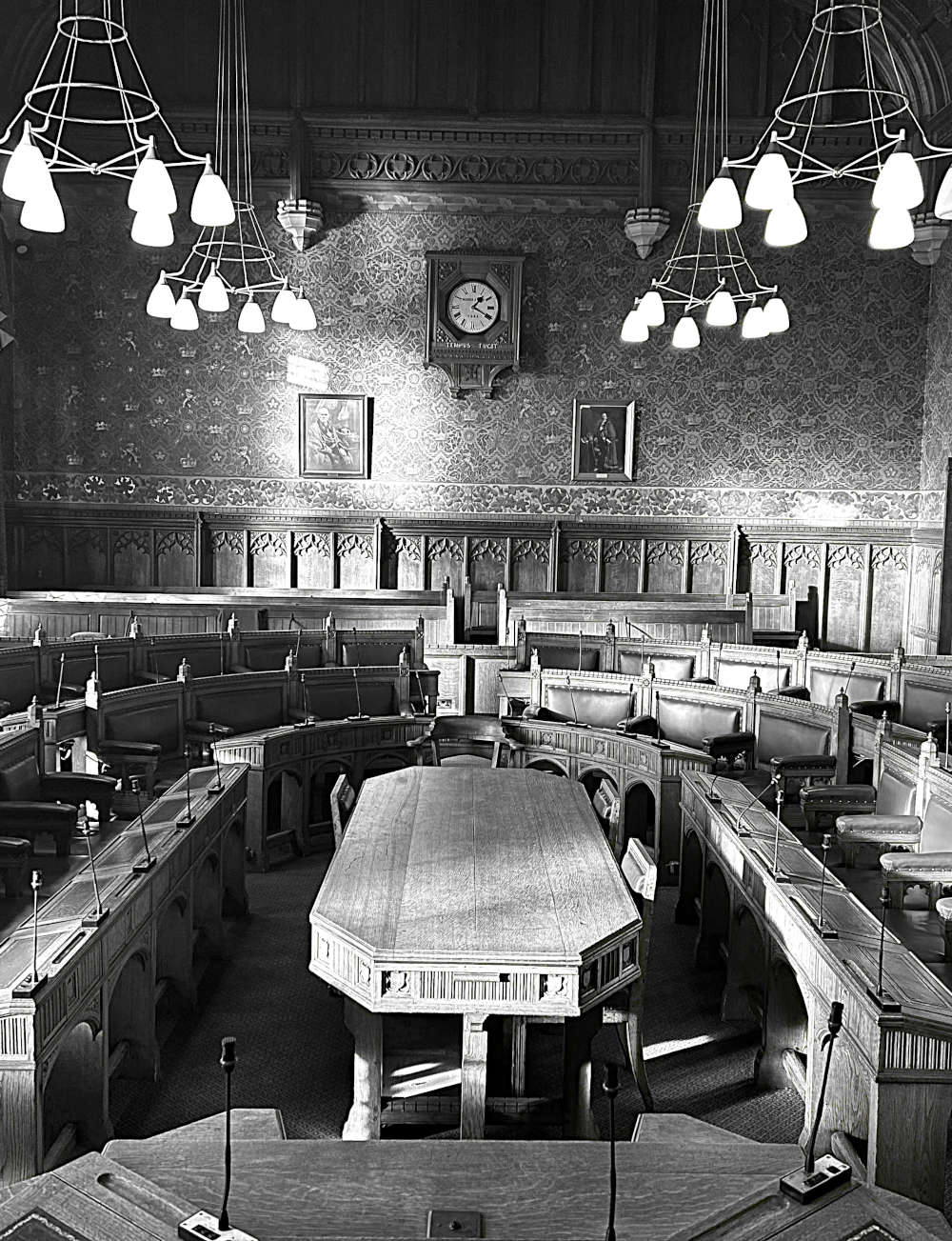 The Guildhall York wedding venue chamber, a black and white photo, showing a grand room with wooden seating, panelled walls and hanging lighting