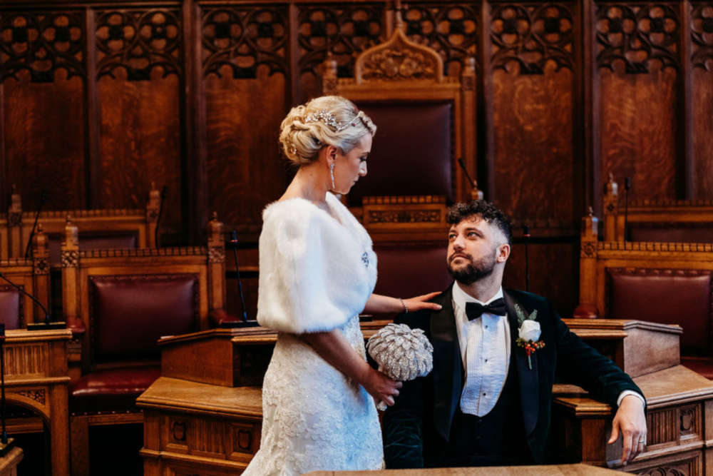 The Guildhall in York wedding venue main hall set out for dining. Photo taken from within the large open hall, a large space with large pillars, a timber ceiling and stain glass windows. Dining tables and seating are set out on the stone floor.