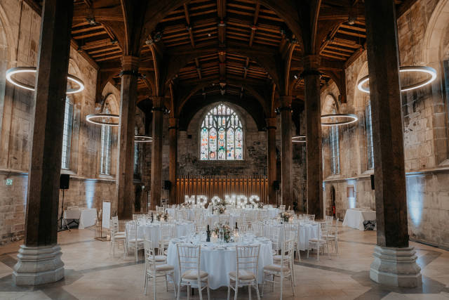 The Guildhall in York wedding venue ceremony room. Photo shows a couple, the groom sitting and the bride standing next to him in a timber panelled room.